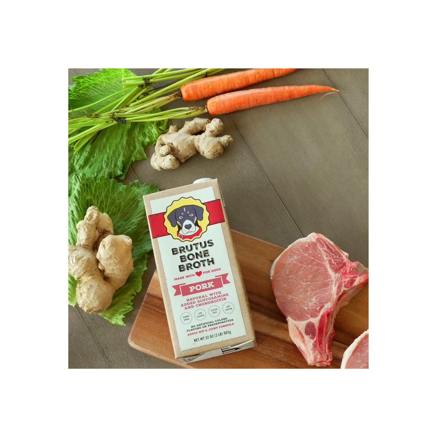 Pork Brutus Bone Broth box lying on a cutting board with raw carrots, ginger, lettuce, pork, and potatoes around it.